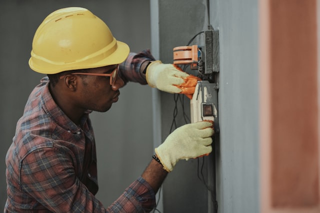Technician in a hard hat repairing a wall-mounted electrical unit